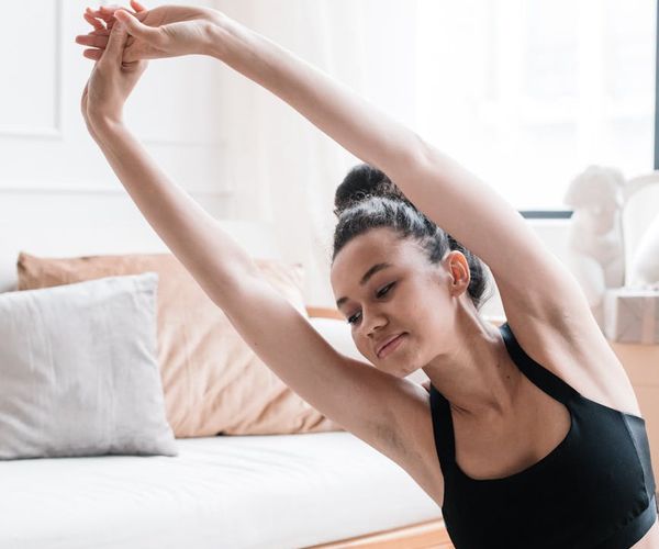 Person stretching peacefully by a large window at sunrise, symbolizing balance and well-being.